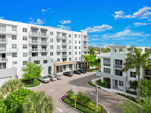A sunny day at a white apartment complex with cars parked in the driveway.