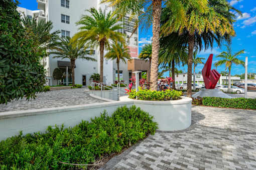 A sculpture of a red bird is in the foreground of a courtyard with palm trees and a white building in the background.