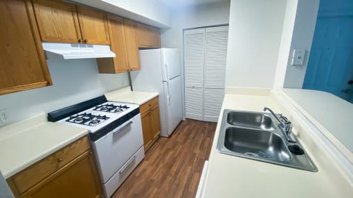 Kitchen featuring brown wood cabinets, white appliances, white countertop, breakfast bar overlooking living room gas stove, and door leading to laundry room in the background