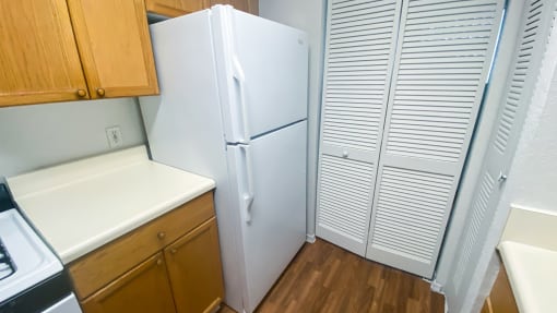 Kitchen featuring brown wood cabinets, white appliances, white countertop, gas stove, pantry and door leading to laundry room in the background