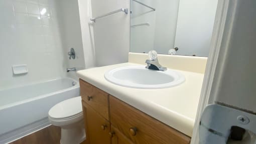 Bathroom with wood floors, toilet, shower tub combo with tile back splash, towel bar and brown wood cabinets