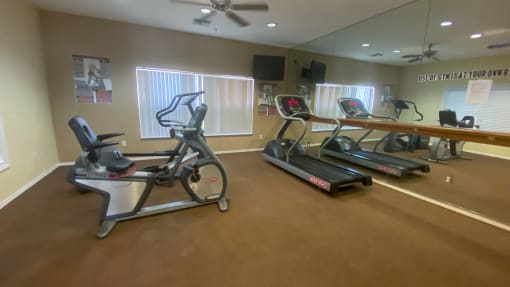 Fitness center with mirrored wall, treadmill, exercise bike, and tv mounted on wall