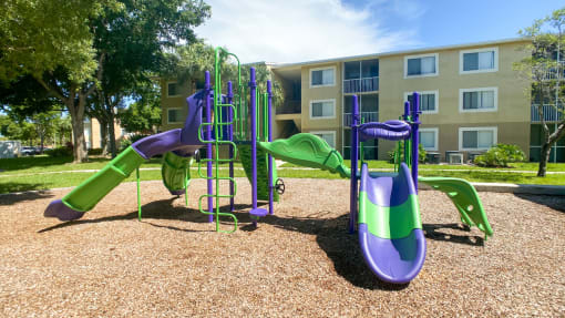 Purple and Green Playground on Mulch with Building Exterior in the Background