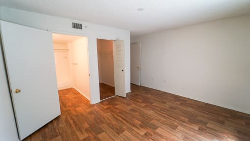 Bedroom with Hardwood Style Flooring and Open Empty Closet Next to En Suite Bathroom