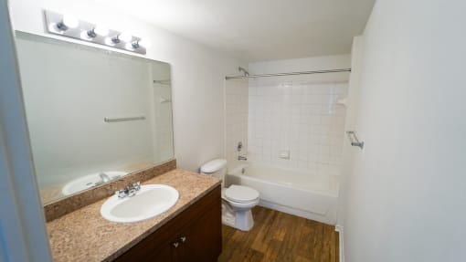 Bathroom with Tan Counters, Wood Cabinets and Toilet Next to White Tiled Shower with Bathtub