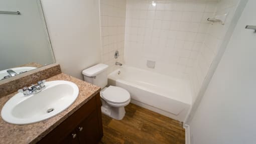 Bathroom with Tan Counters, Wood Cabinets and Toilet Next to White Tiled Shower with Bathtub