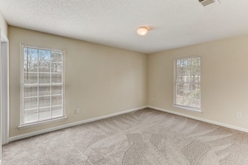 an empty living room with carpet and two windows