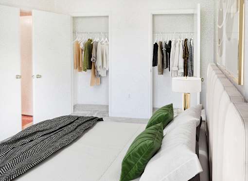 A bedroom with a bed, pillows, and a closet with clothes hanging.