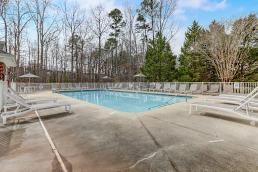 our resort style swimming pool is surrounded by white chairs and trees