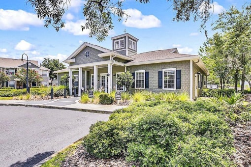 Clubhouse exterior with pavers leading to the office with bushes and trees in front of them