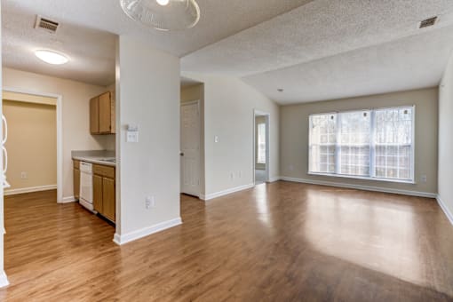 an empty living room and kitchen with wood flooring and a large window