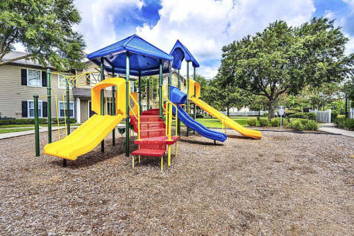 Outdoor playground with two yellow slides, a blue slide, and several climbing areas.