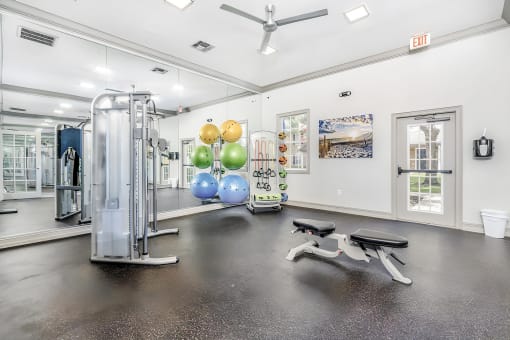 Fitness room with strength and cardio equipment, mirrors, windows, and a ceiling fan.