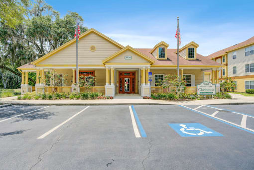 Exterior of clubhouse and parking lot with two flag poles, community sign and native landscaping