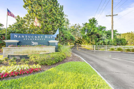 Community Entrance Sign Next to Two Lane Road Shaded by Trees
