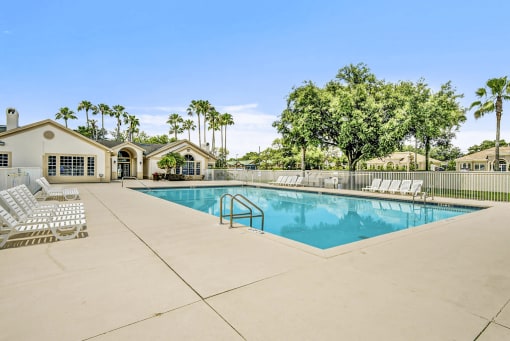 Swimming pool with large tanning deck, green trees, and building exterior in the background
