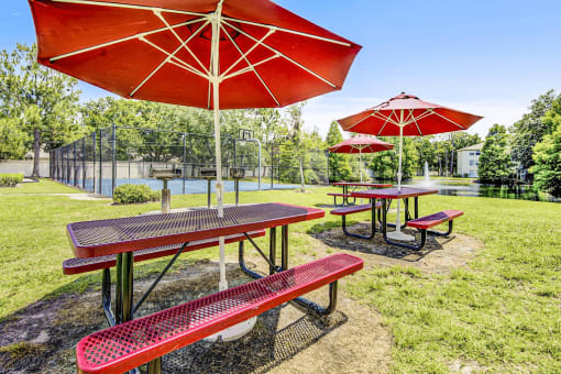 Grill area featuring red picnic tables with red umbrellas overlooking the fountain and basketball court