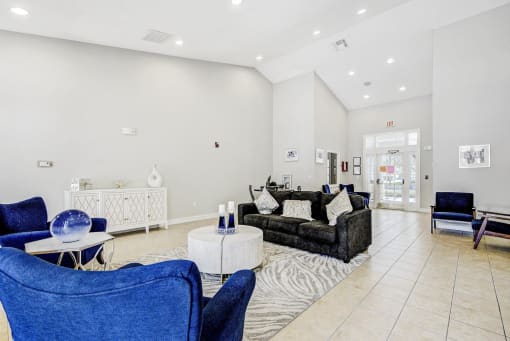 Clubhouse Seating Area with Area Rug, Couch, Coffee Table and Armchairs with Leasing Office Entry with French Doors, Armchairs and Dining Table with Chairs in the Background