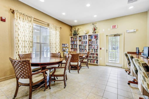 Business Center with Dining Tables with Chairs, Built in Desk with Computers, monitors and Office Chairs Next to Fully Stocked Bookshelves