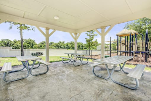 A pergola with three picnic tables and a BBQ grill near the playground.