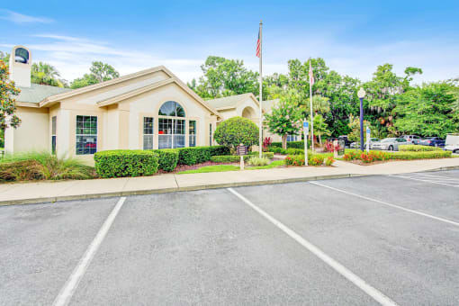 Clubhouse Entrance surrounded by shrubbery and trees with view of parking lot