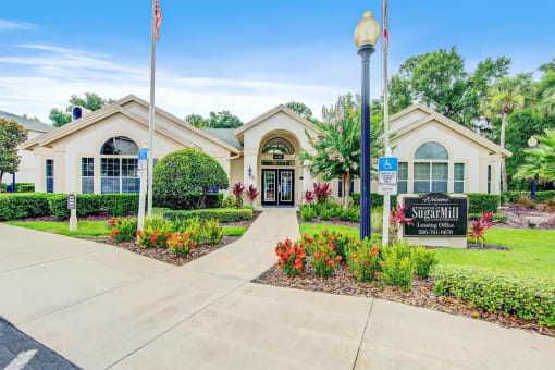 Clubhouse Entrance surrounded by shrubbery and trees with monument sign in front of it