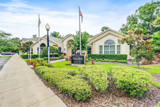Clubhouse Entrance surrounded by shrubbery and trees with monument sign in front of it
