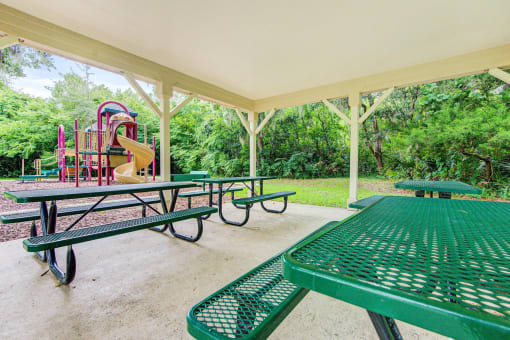 A pergola over 4 picnic tables near the playground equipment.