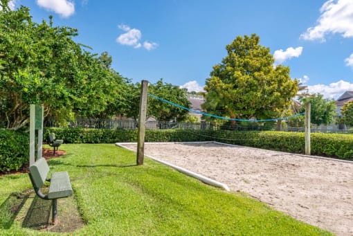 Sand Volleyball Court with Nearby Bench Surrounded by Trees and Shrubs with Building Exterior in The Background
