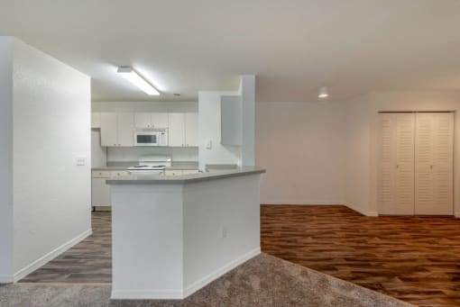 Open Kitchen with Grey Counters White Appliances and Cabinets with Breakfast Bar Next to Dining Room with Hardwood Style Flooring with Sliding Closet