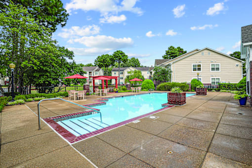 A swimming pool surrounded by a concrete patio and a red umbrella.