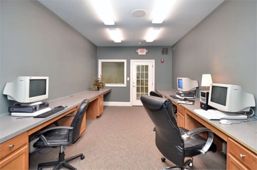 Community business center with multiple monitors and desktop computers. Black rolling chairs sit at each work station