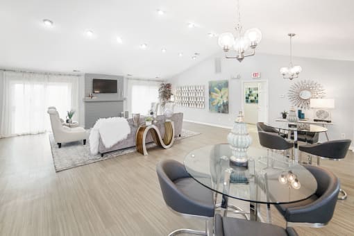 Clubroom seating with couch and accent chairs around tv. Also in background two 4-top dining room glass tables
