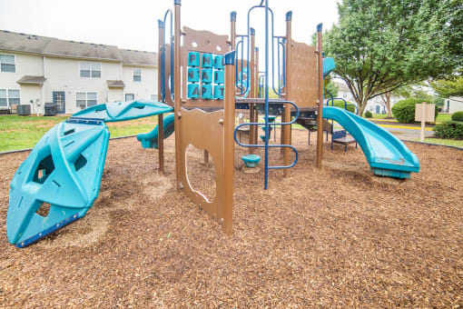 Playground jungle gym and playground slides in a bed of mulch with building and trees in background