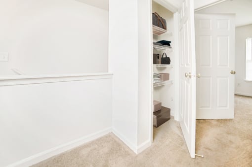 Carpeted hallway with linen closet, virtually staged with clothes. Leading to bedroom in background
