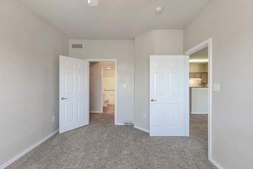 A room with carpeted floor and three white doors.