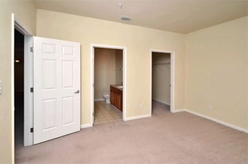 Vacant bedroom with tan carpet and beige walls. The bathroom and closet are in the back of the room.