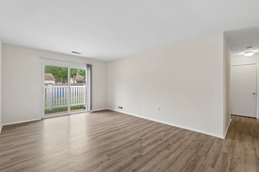 A room with wooden floors and white walls, with a sliding glass door leading to a balcony.