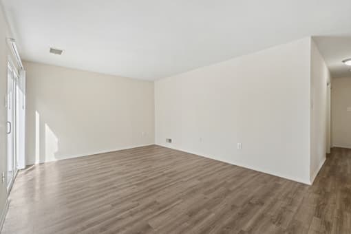 A large empty room with wooden flooring and white walls.