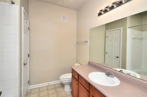 Vacant bathroom with linoleum flooring and beige walls. A shower is on the left side with a sink on the right.