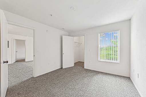 A room with a carpeted floor and a window with a view of a fence.