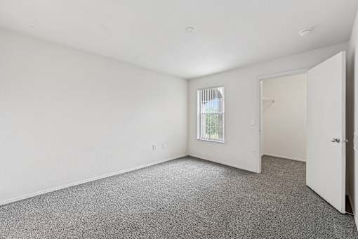 A room with a carpeted floor and a window with blinds.