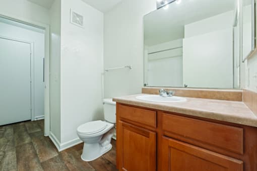 A white toilet sits in a bathroom with wooden floors and a wooden vanity.