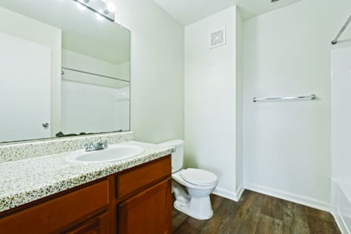 A white toilet sits in a bathroom with a marble counter and wooden floors.