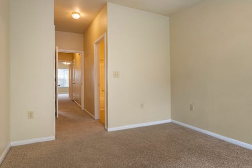 a spacious living room with carpeting and a hallway to a bedroom