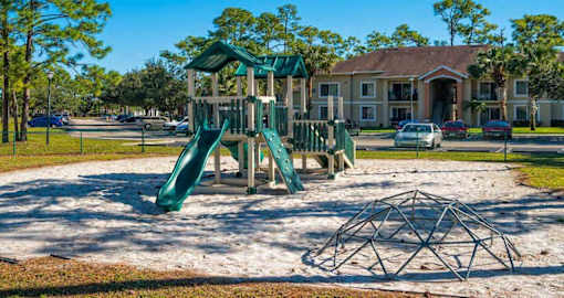 Fenced in Playground on Sand with Parking Lot and Building  in the Background