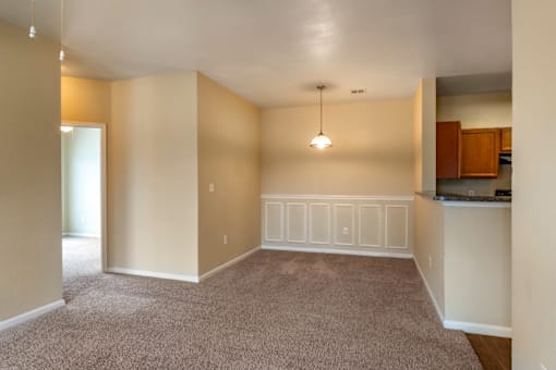 an empty living room with a kitchen in the background