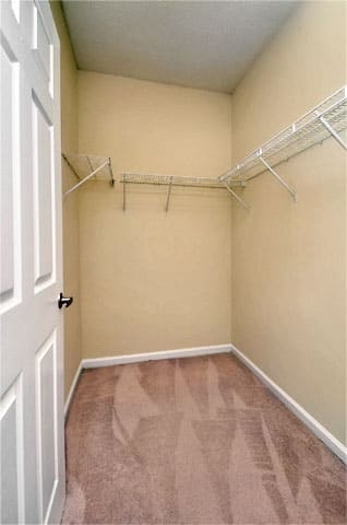 Vacant closet with wire shelving, tan carpet, beige walls, and ceilings throughout.
