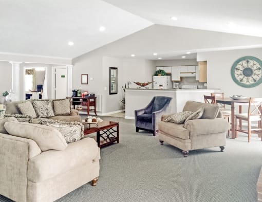 The resident clubhouse features ample seating including a couch, loveseat, and two chairs There is a white fireplace with a television mounted above it.. The room features gray carpet with beige walls that are set against a white textured ceiling with recessed lighting