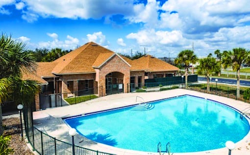 A swimming pool in front of a house with a fence around it.